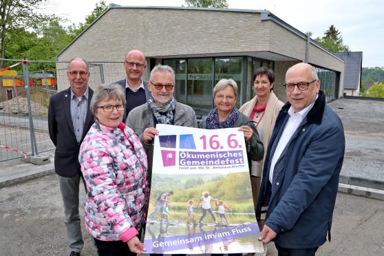 Präsentierten das Plakat zum ersten gemeinsamen Gemeindefest der evangelischen und der katholischen Kirche in Wickede (Ruhr): der evangelische Pfarrer Dr. Christian Klein und sein katholischer Kollege Thomas Metten sowie die Pfarrgemeinderatsmitglieder Felizitas Vollmer, Helmut Rubarth und Lydia Münstermann sowie Prädikantin Eva Berneis und Stefan Dittrich vom Fest-Komitee der evangelischen Kirchengemeinde. Im Hintergrund: das katholische Franziskus-Forum und die Baustelle darum. FOTO: ANDREAS DUNKER