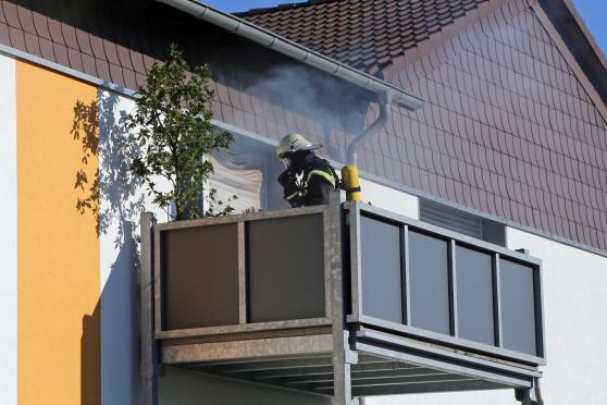 Qualm kommt aus der brennenden Wohnung im Wickeder Osten. Ein Feuerwehrmann mit Atemschutz steht auf dem Balkon. FOTO: CARINA WESTERWELLE