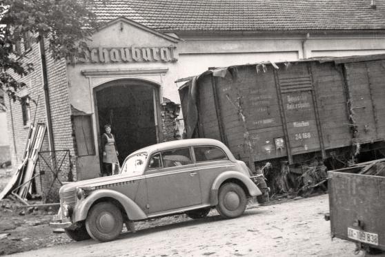 Ein von der Flutwelle der Möhnekatastrophe bis auf die Hauptstraße in Wickede geschwemmter Eisenbahnwagon. – Dies zeigt, welch zerstörerische Wucht die Wasserwelle im Möhne- und Ruhrtal hatte. – Im Hintergrund das zerstörte Kino "Schauburg" neben der Gaststätte Lindenhof. ARCHIVFOTO